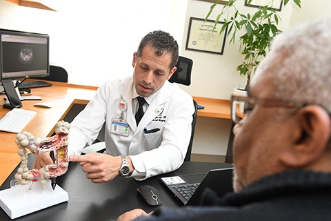 Dr. Zoccali seated at his desk across from a patient as he is pointing out anatomical structures and evidence of disease on a model of the colon.